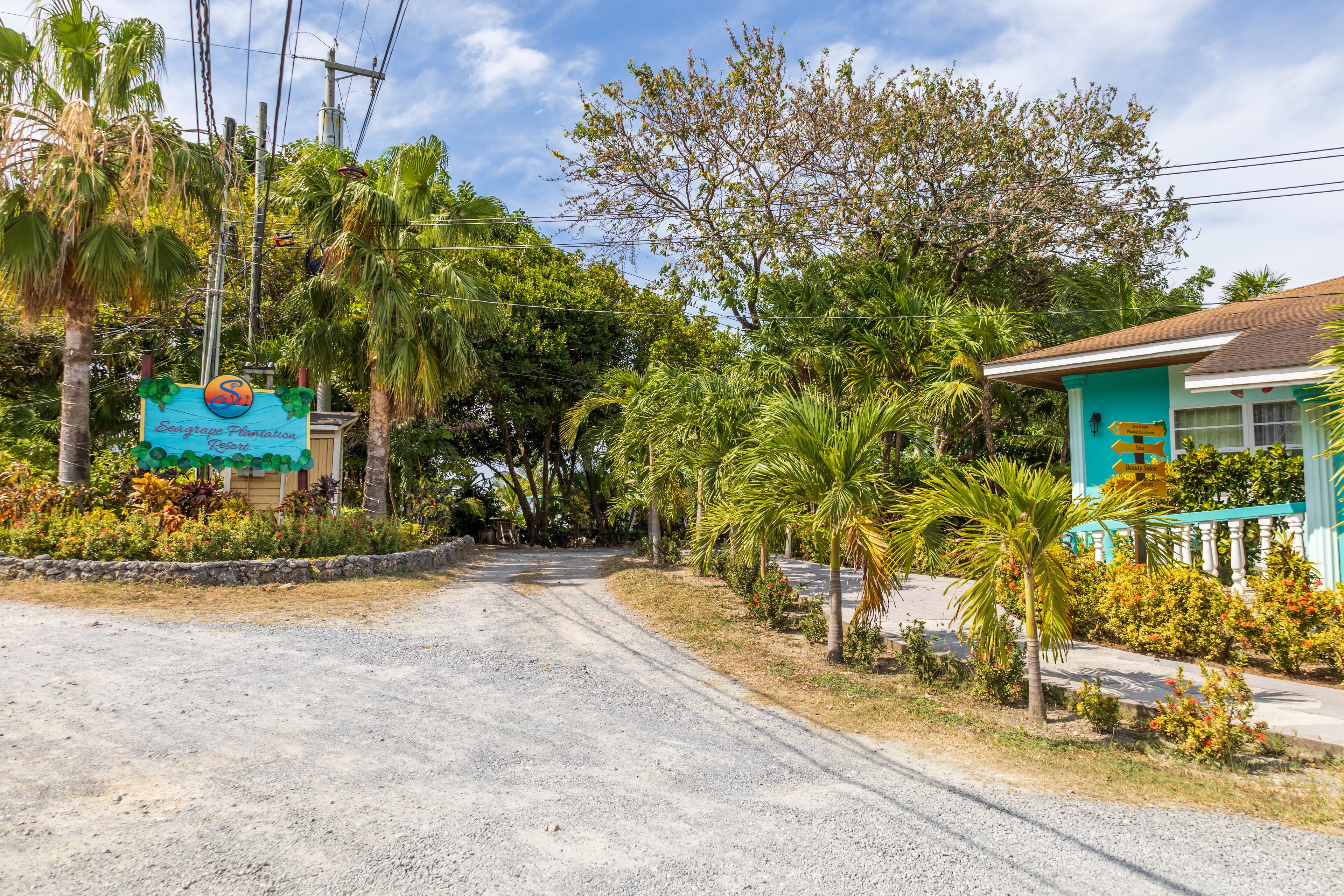 Un panneau indiquant le « Seagrape Plantation Resort », une route menant à un bâtiment à la façade turquoise, entouré d’une végétation tropicale.
