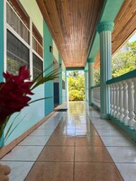 Un pasillo con techo de madera, suelo de baldosas y columnas con barandillas.