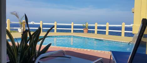 Una piscina con cerramiento blanco y plantas en macetas, con vistas a una extensión de agua.