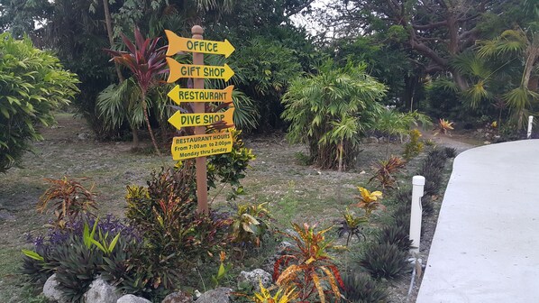 A signpost with directions to an office, gift shop, restaurant, and dive shop. - Seagrape Plantation Resort (Roatan)