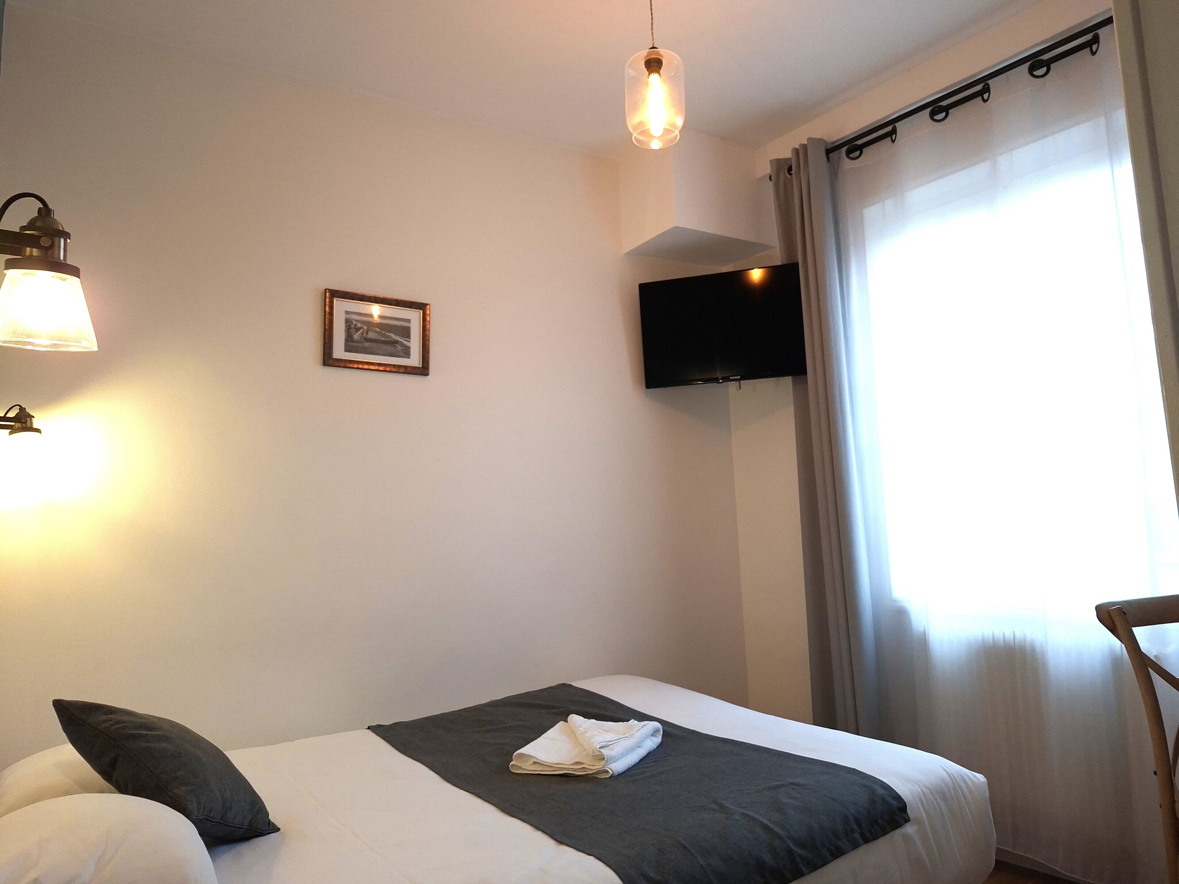 Ein Hotelzimmer mit Bett, einem wandmontierten Flachbildfernseher, einem gerahmten Bild und einem Fenster mit Vorhängen.