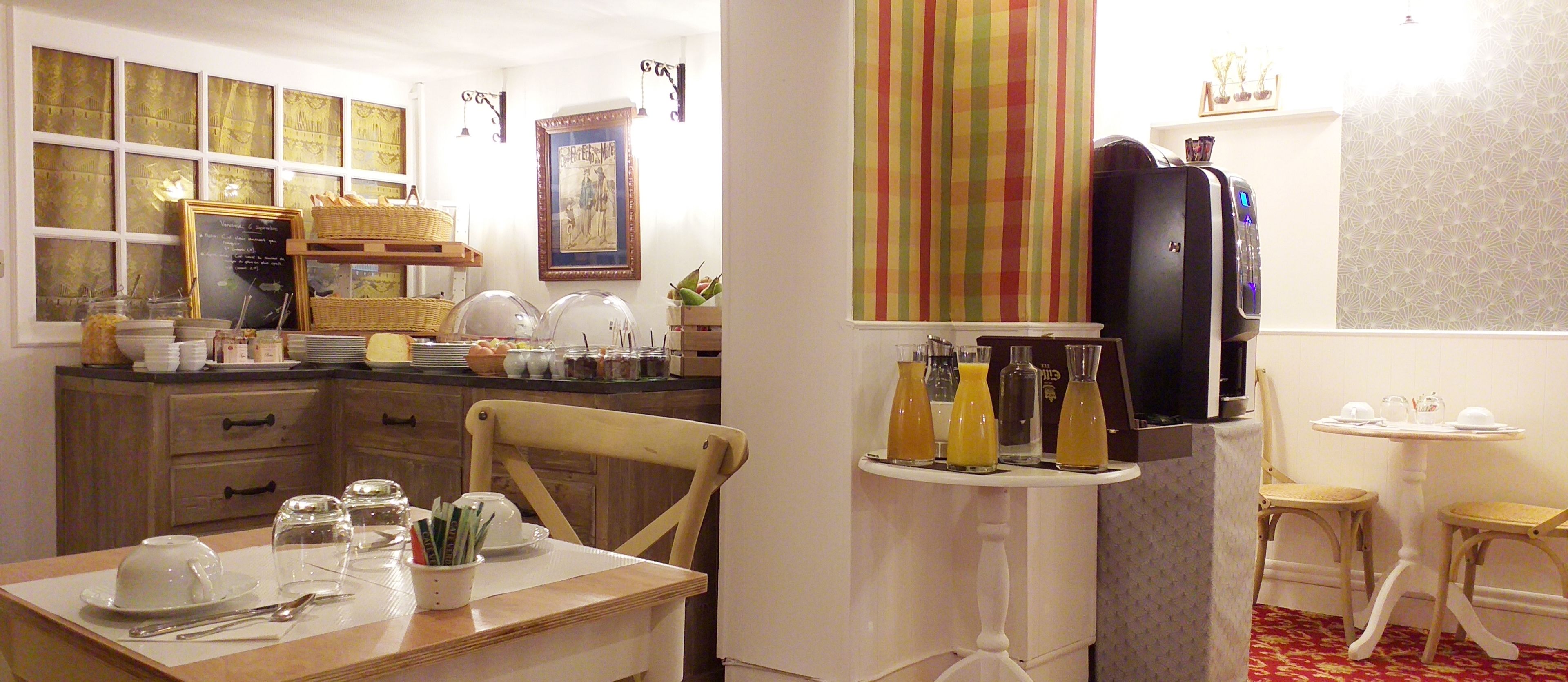 Una cocina bien iluminada con armarios de madera, una mesa de comedor con platos y cubiertos, un refrigerador y una mesita con algunos objetos encima.