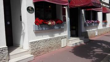 A hotel facade with red awnings, flower boxes with red and pink flowers, and a stone wall.
