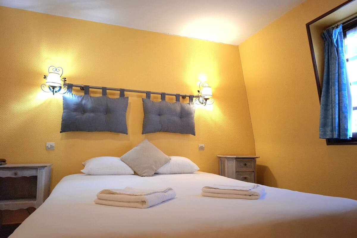 Une chambre d’hôtel avec un lit, deux lampes fixées au mur, une table de chevet et une fenêtre avec des rideaux.