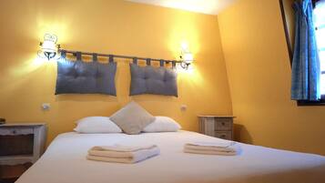Habitación de hotel con cama, dos lámparas de pared, una mesita de noche y una ventana con cortinas.