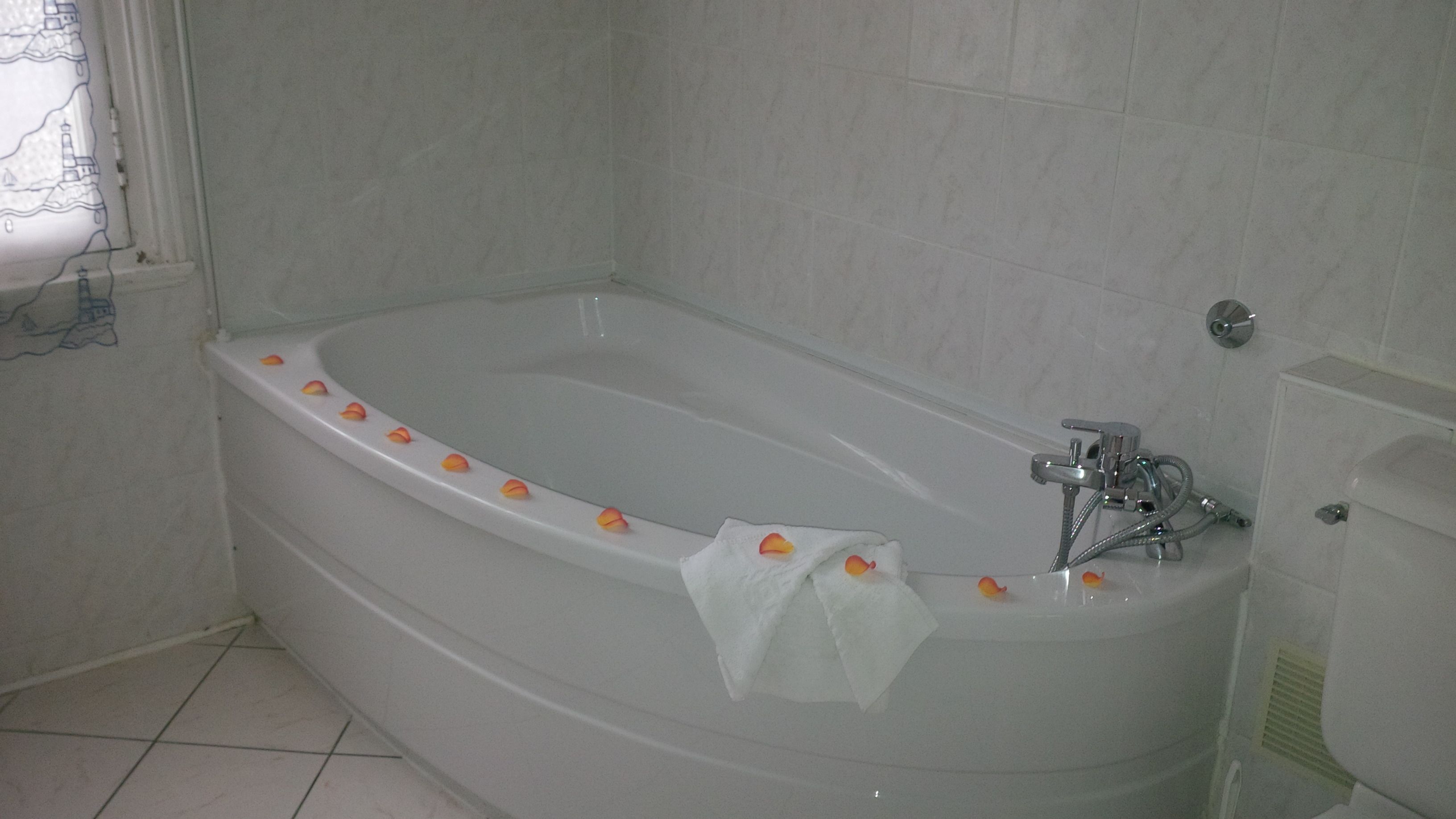 Eine Standardbadewanne mit Duschbrause, einem Handtuch und Rosenblüten am Rand.