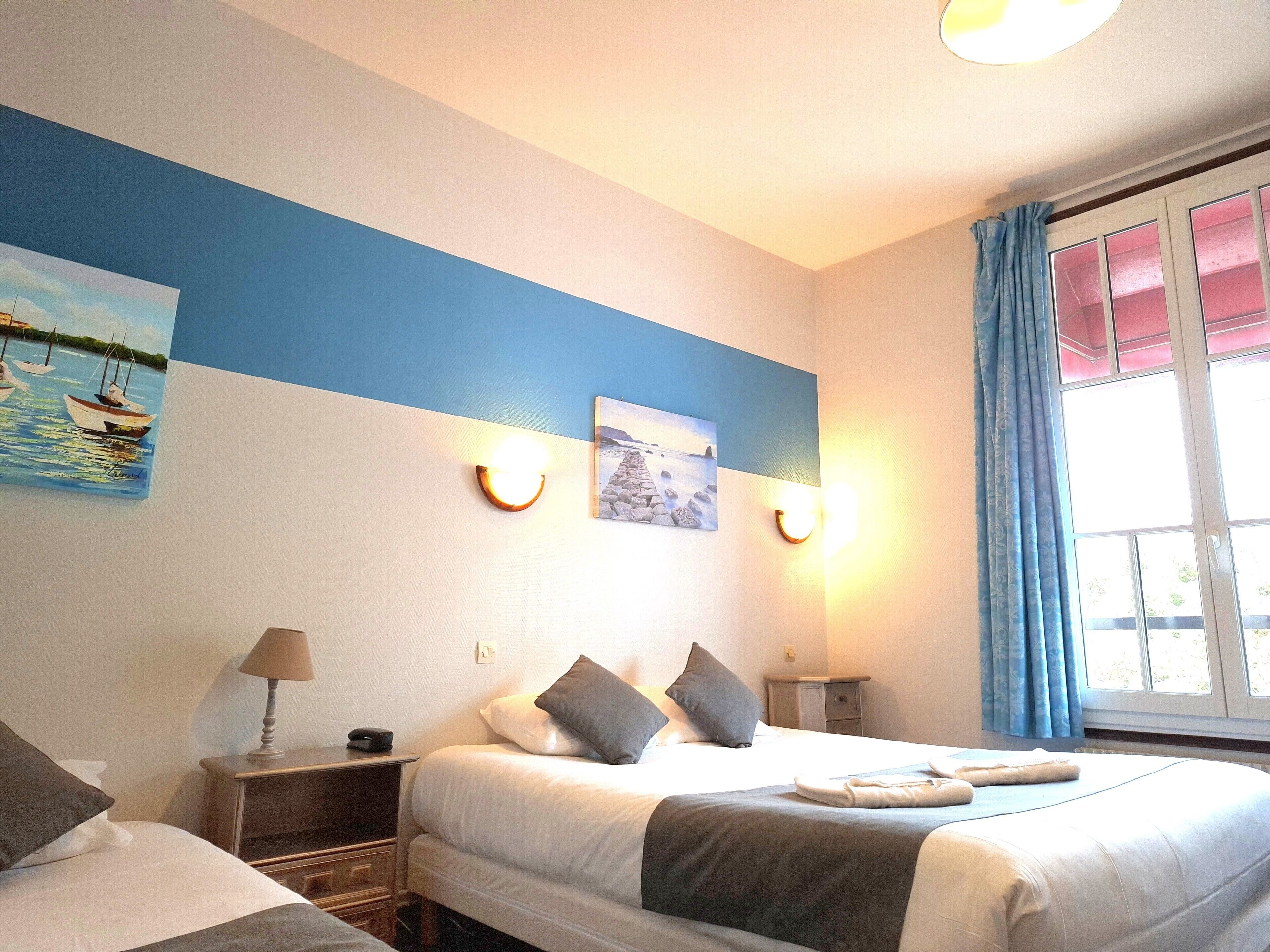 Habitación de hotel con dos camas, una mesita de noche con lámpara, un cuadro en la pared y una ventana con cortinas.