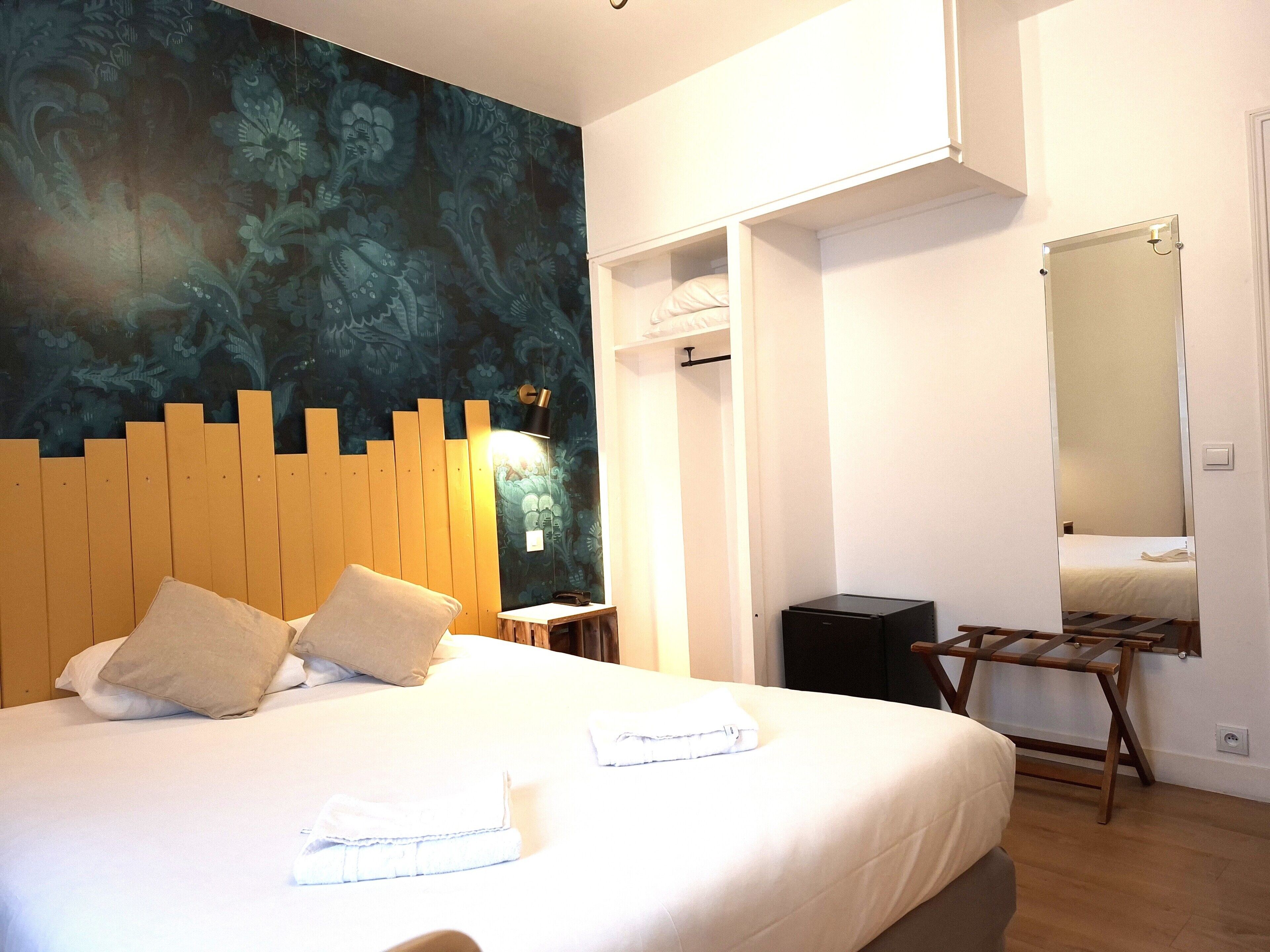 A hotel room with a bed, a wooden headboard, a wall-mounted mirror, and a wardrobe.