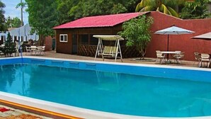A swimming pool with a red-roofed building, a covered seating area, and a small structure with a window. - Hotel Taciana (Léogâne)