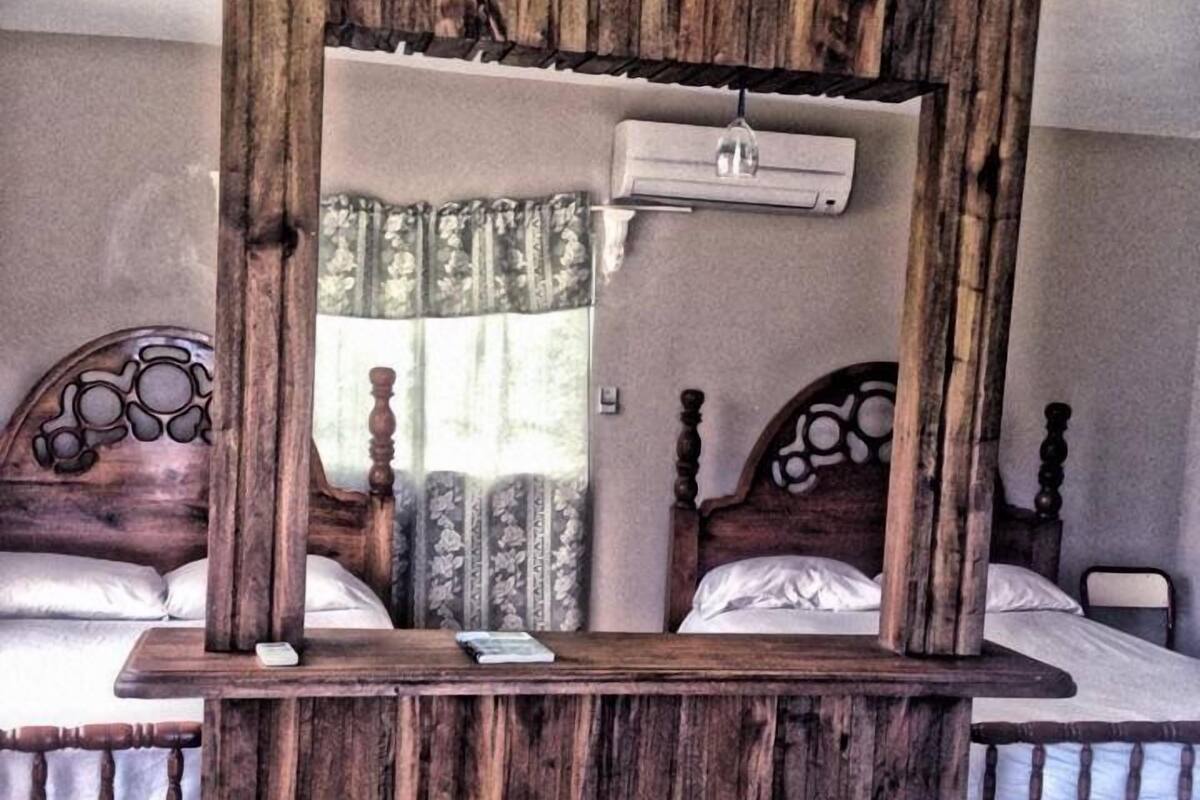 Ein rustikaler Holzerspiegel in einem Hotelzimmer mit zwei Betten, jeweils mit einem Holz-Kopfteil und einer weißen Matratze.