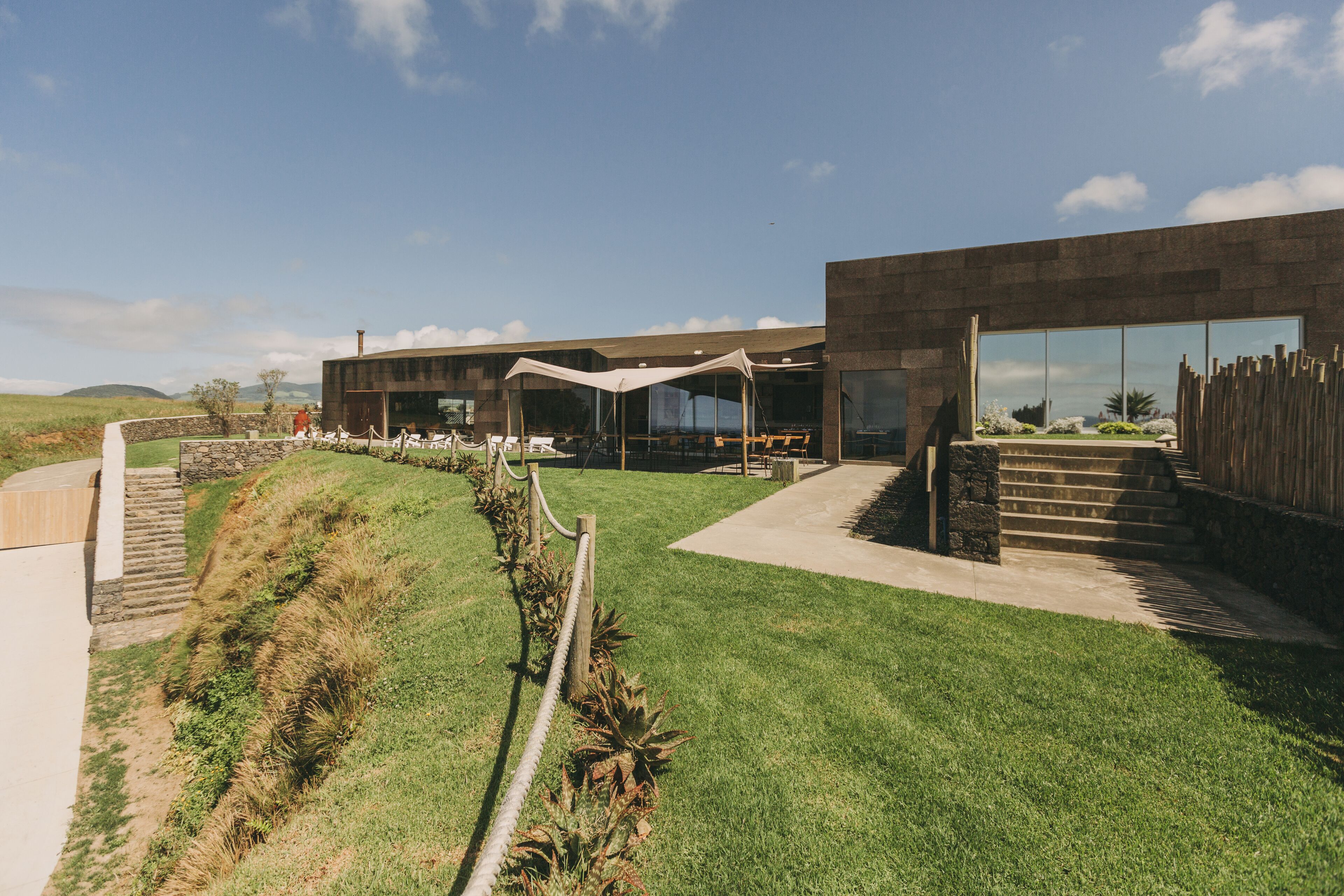 A modern building with a flat roof, large windows, and a grassy area with a pathway leading to the entrance.