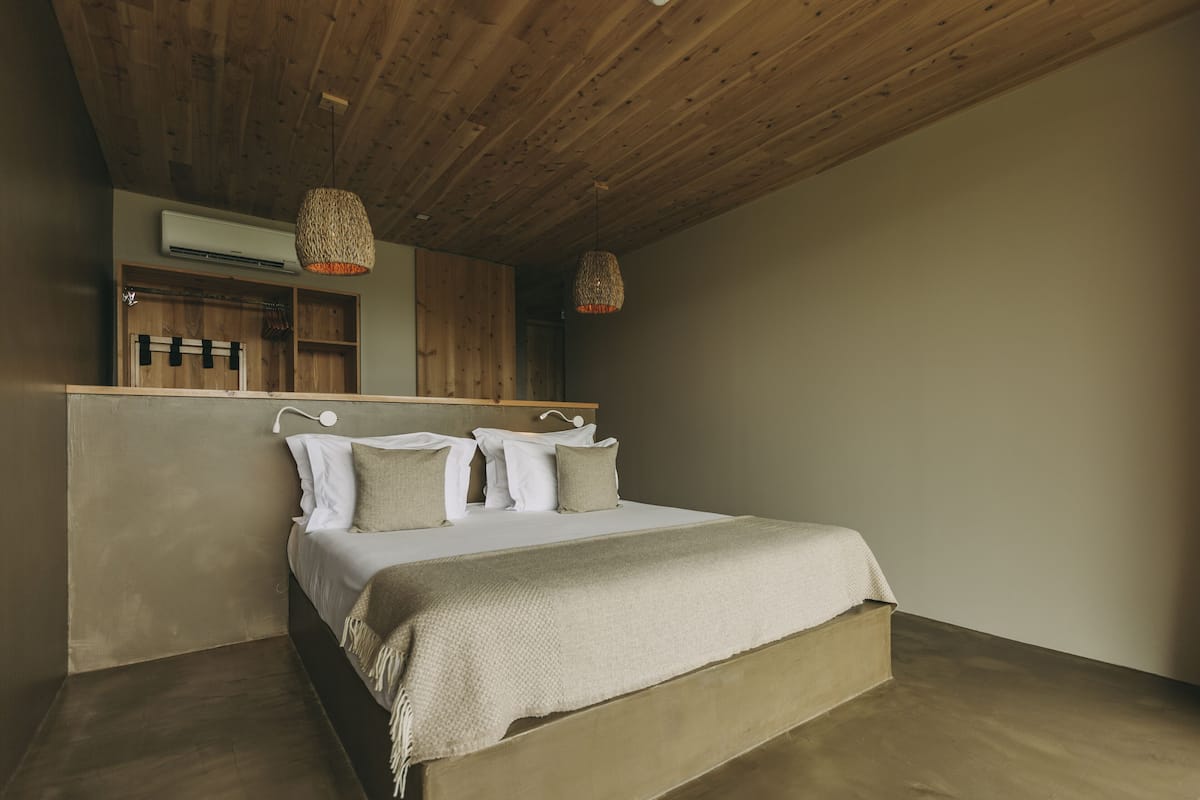 Een slaapkamer met een houten plafond, een bed met witte beddengoed, twee hanglampen en een inbouw kast.