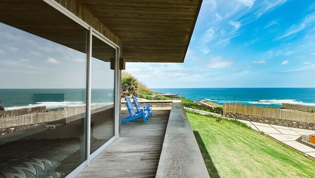 Une maison moderne avec une porte vitrée donnant sur un balcon qui offre une vue sur l’océan.