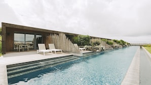 Un espace piscine moderne avec une eau cristalline, une terrasse en bois et des chaises longues.