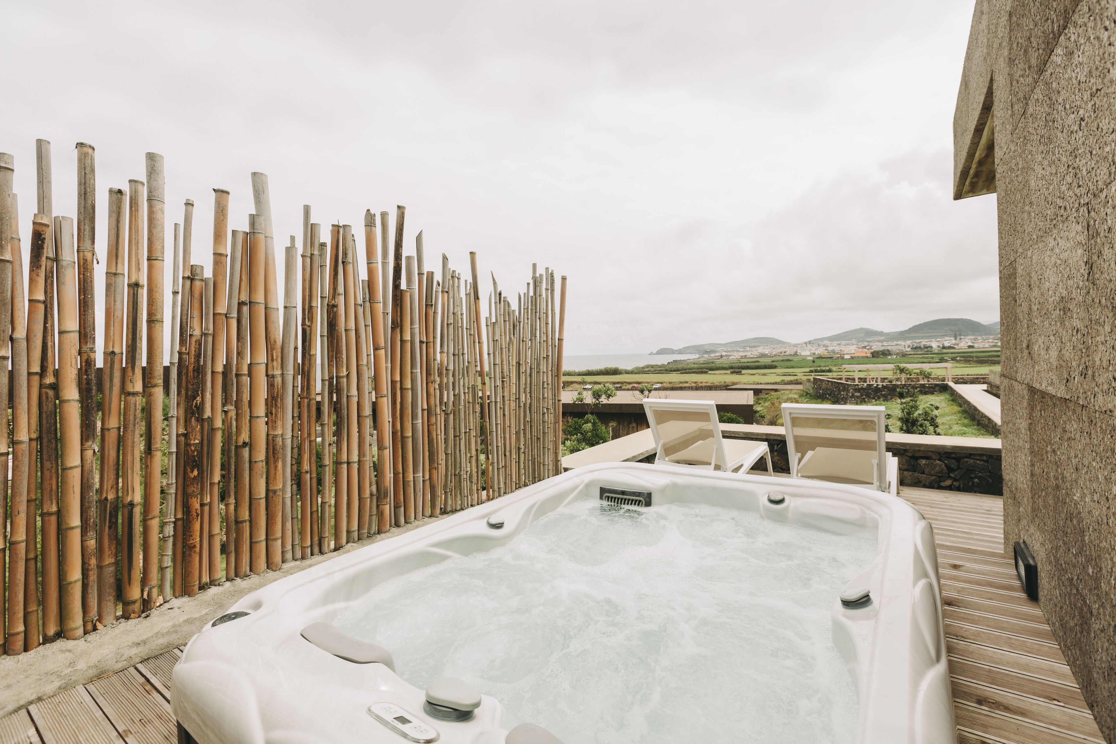 A hot tub on a wooden deck with a bamboo fence and a view of the countryside.