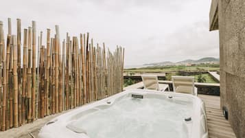 A hot tub on a wooden deck with a bamboo fence and a view of the countryside.