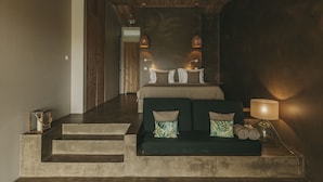 Une chambre d’hôtel moderne avec un plafond en bois, un lit doté d’une tête de lit verte, un canapé avec des coussins et une table de chevet avec une lampe.