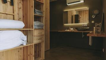 Una habitación de madera con una cama, un estante con toallas dobladas, un lavamanos y un espejo.