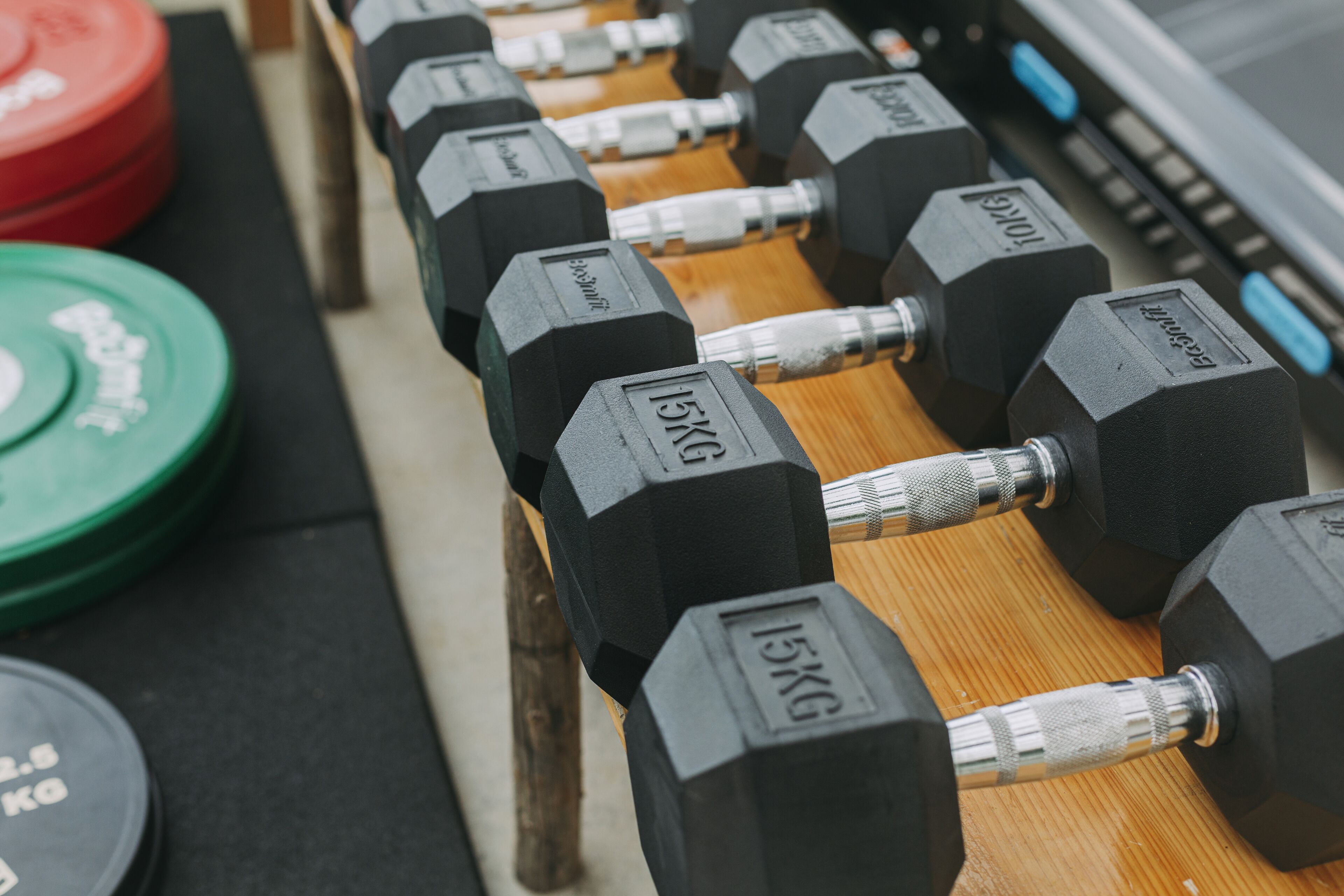 A row of black dumbbells with weight markings on a wooden surface.
