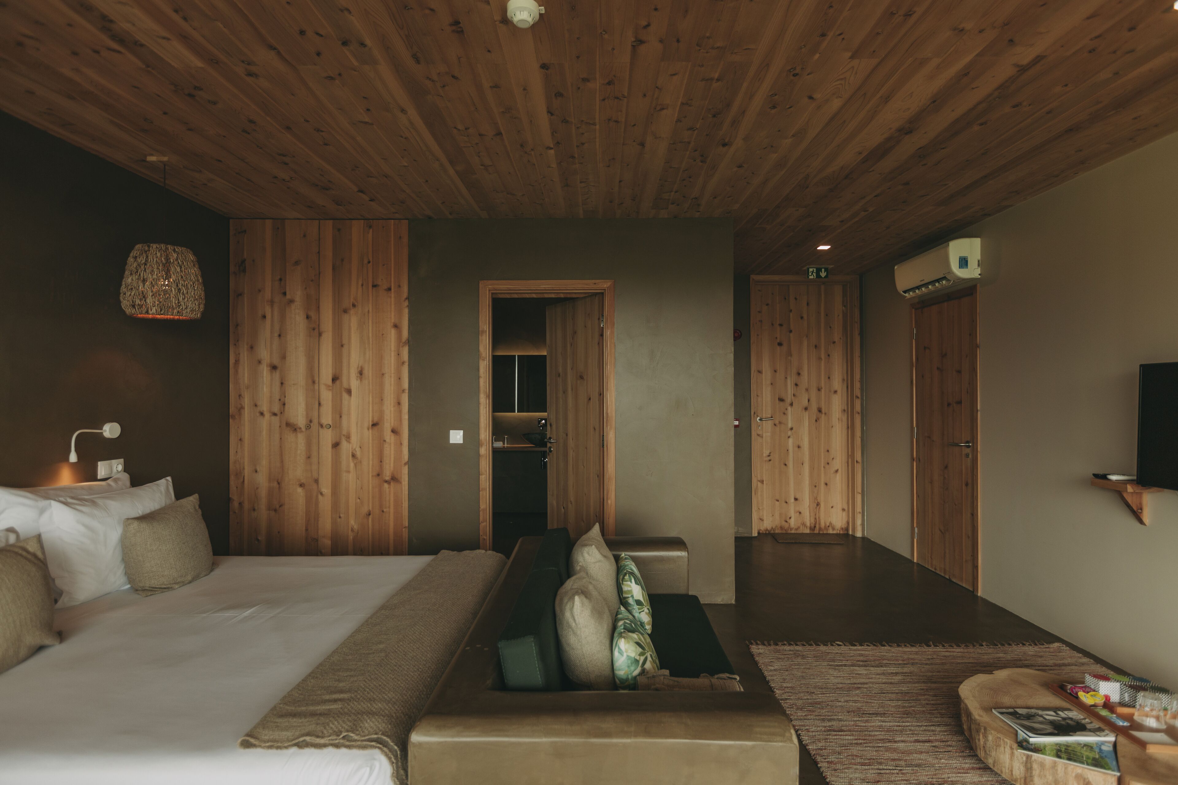 A bedroom with a wooden ceiling, a bed with pillows, a bedside table, and a wall-mounted TV.