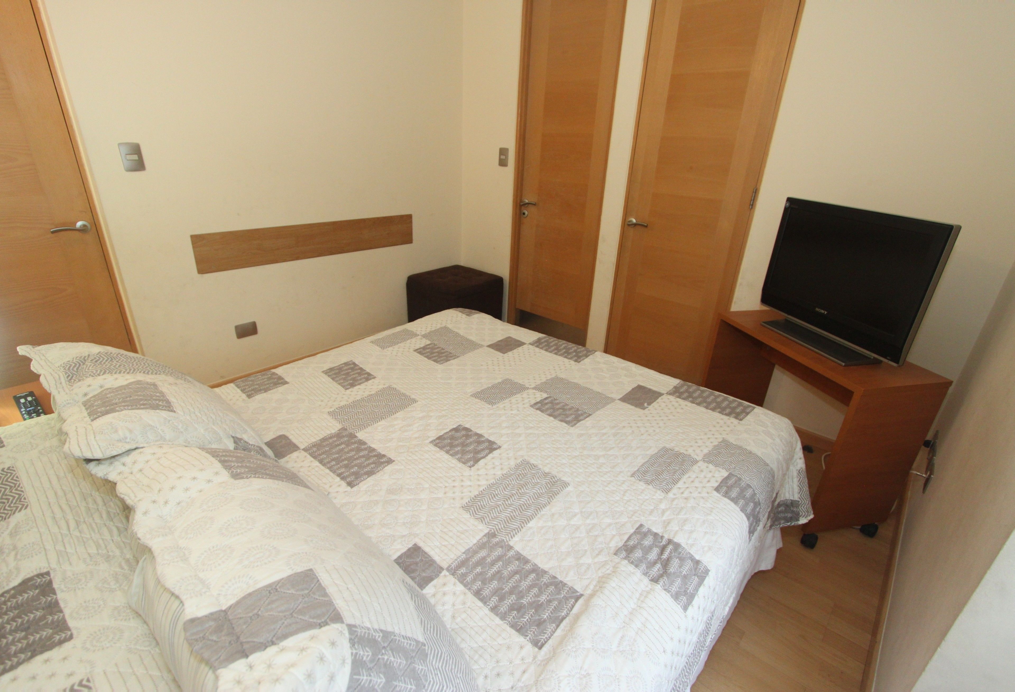 Un dormitorio con una cama, un televisor sobre un mueble bajo y un armario.