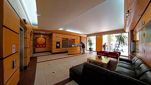 A lobby with a reception desk, a black leather sofa, and a red couch. - Trani Apart Las Condes (Santiago)
