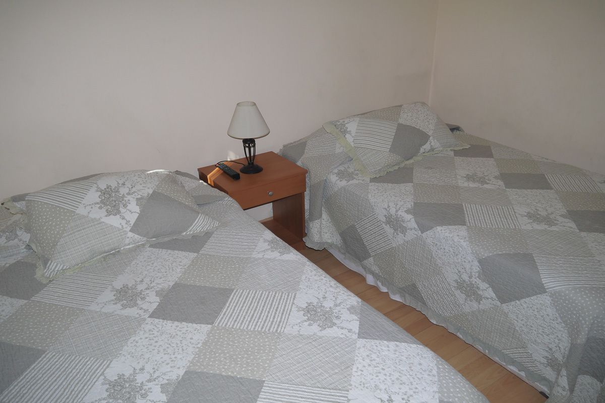 Una habitación pequeña y sencilla con dos camas, una mesita de noche y una lámpara.