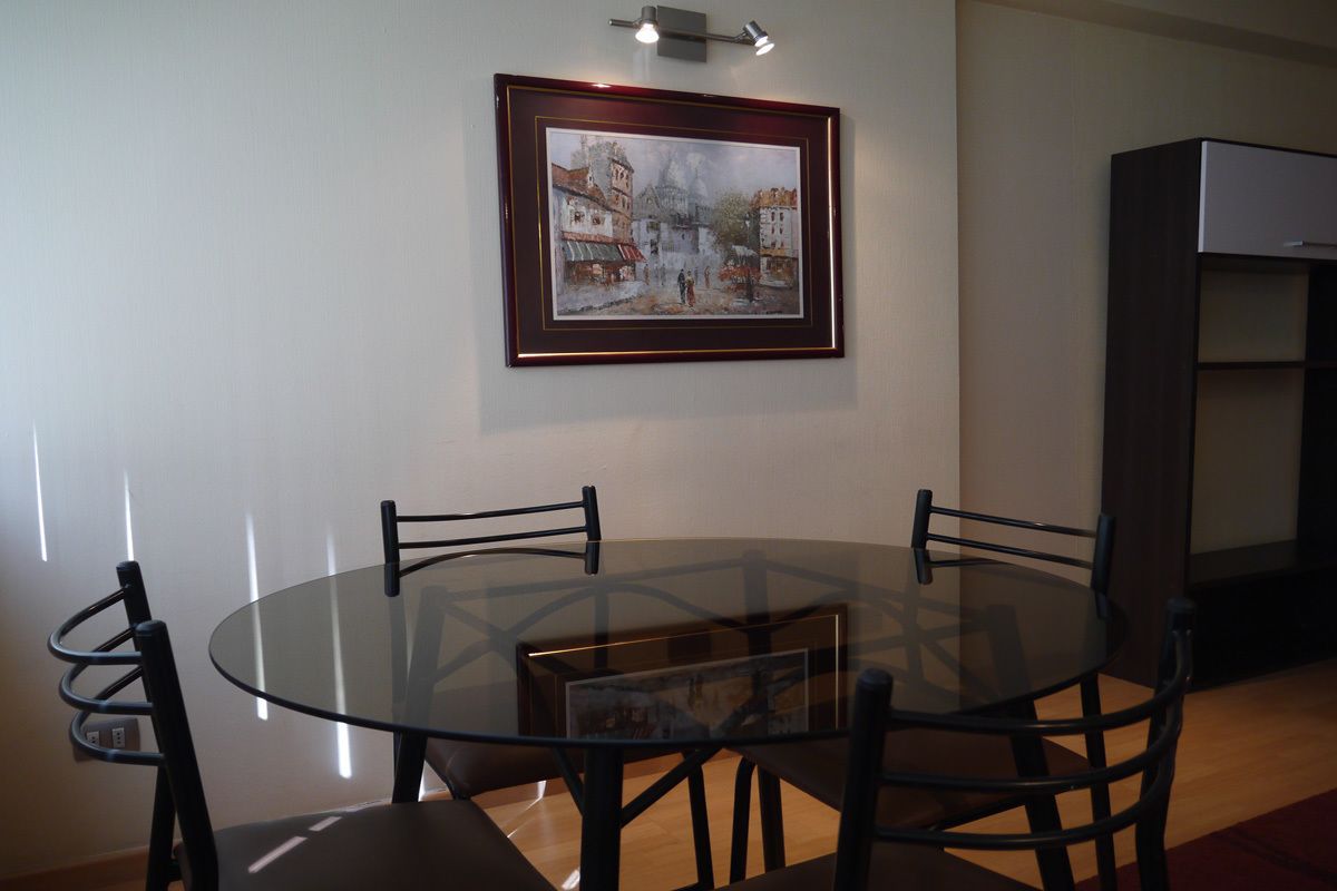 A dining area with a round glass table, black chairs, and a framed painting on the wall.