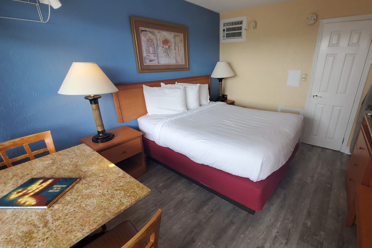 A hotel room with a bed, two bedside tables with lamps, a desk with a chair, a framed picture on the wall, and a door.