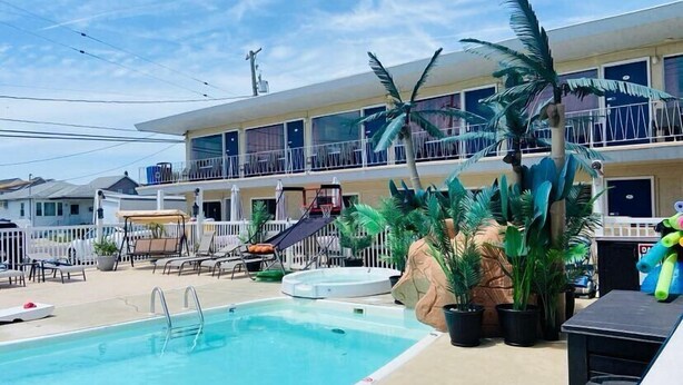 A hotel with a swimming pool, lounge chairs, and a tropical plant arrangement. - Sand Box Motel (Wildwood)