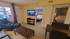 A hotel room with a bed, a desk, a chair, a TV, and a window with curtains. - Sand Box Motel (Wildwood)