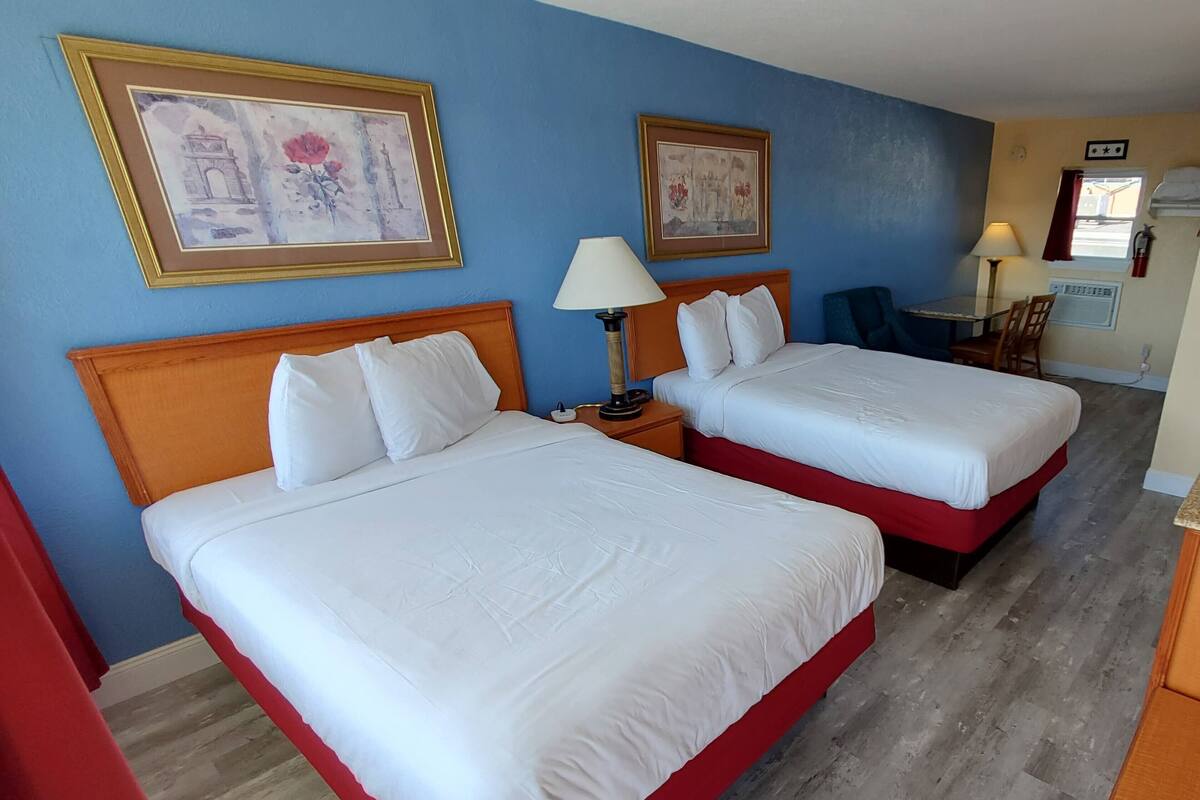A hotel room with two beds, a nightstand with a lamp, and two framed pictures on the wall.