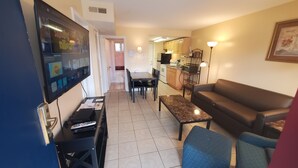 A living room with a TV, a sofa, a coffee table, and a dining area with chairs. - Sand Box Motel (Wildwood)