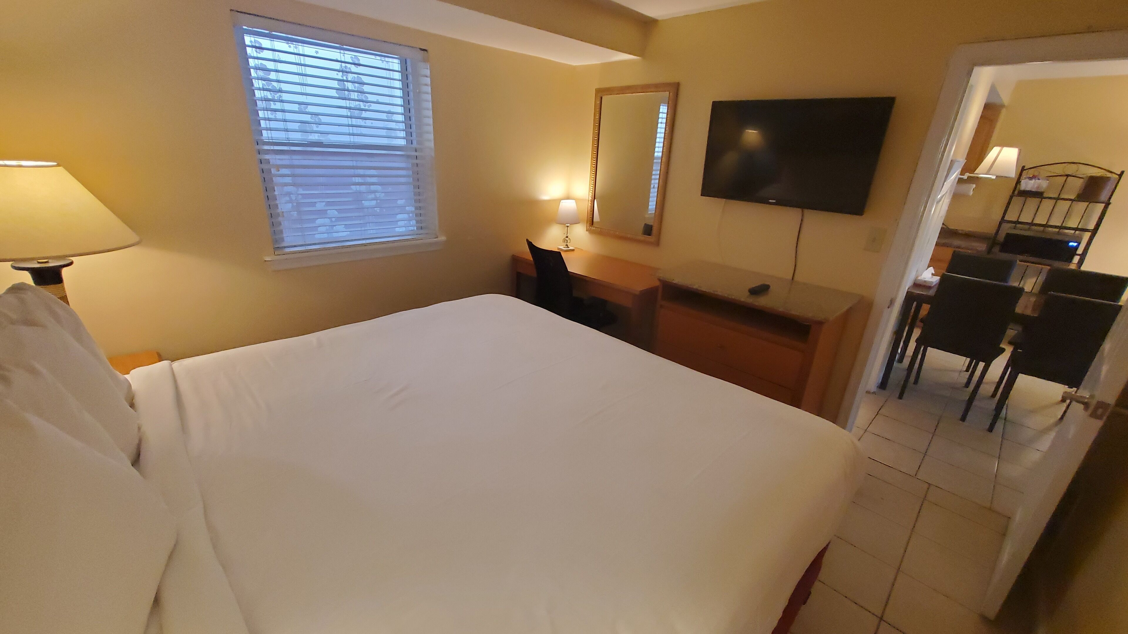 A hotel room with a bed, a desk, a chair, a TV, and a window with blinds.
