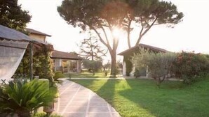 A pathway leading to a building with a covered patio area, surrounded by well-maintained grass and trees. - La Meridiana (Lanuvio)