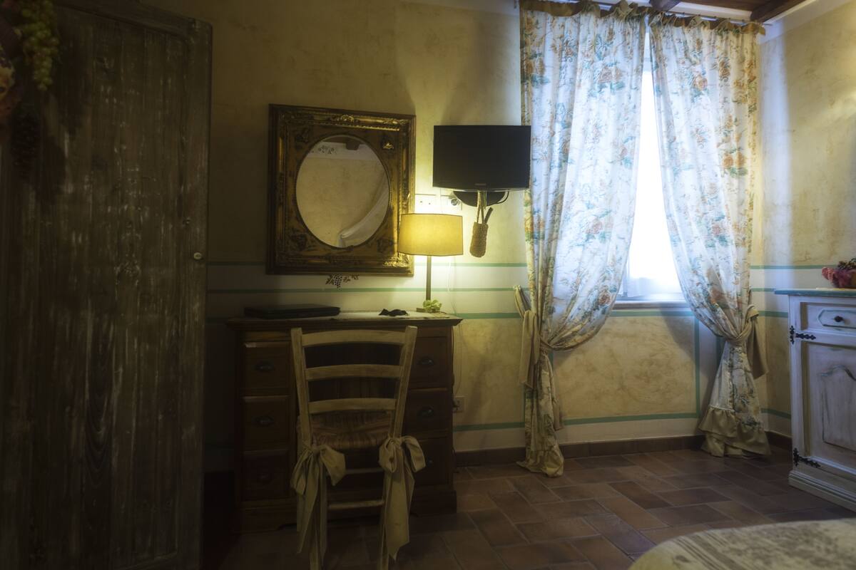 A room with a wooden dresser, a chair, a mirror, a television, and curtains.