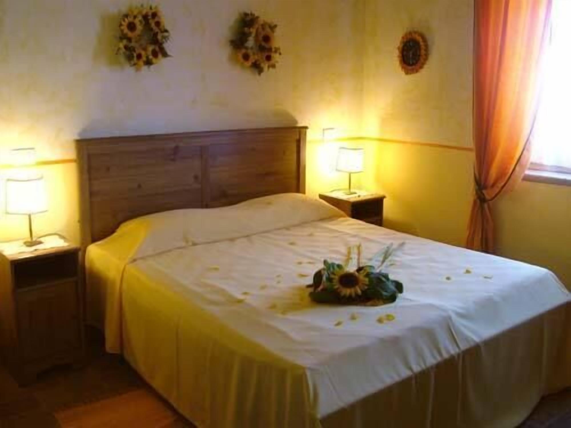 Una cama bien hecha con un arreglo floral, dos lámparas de noche y un reloj de pared.