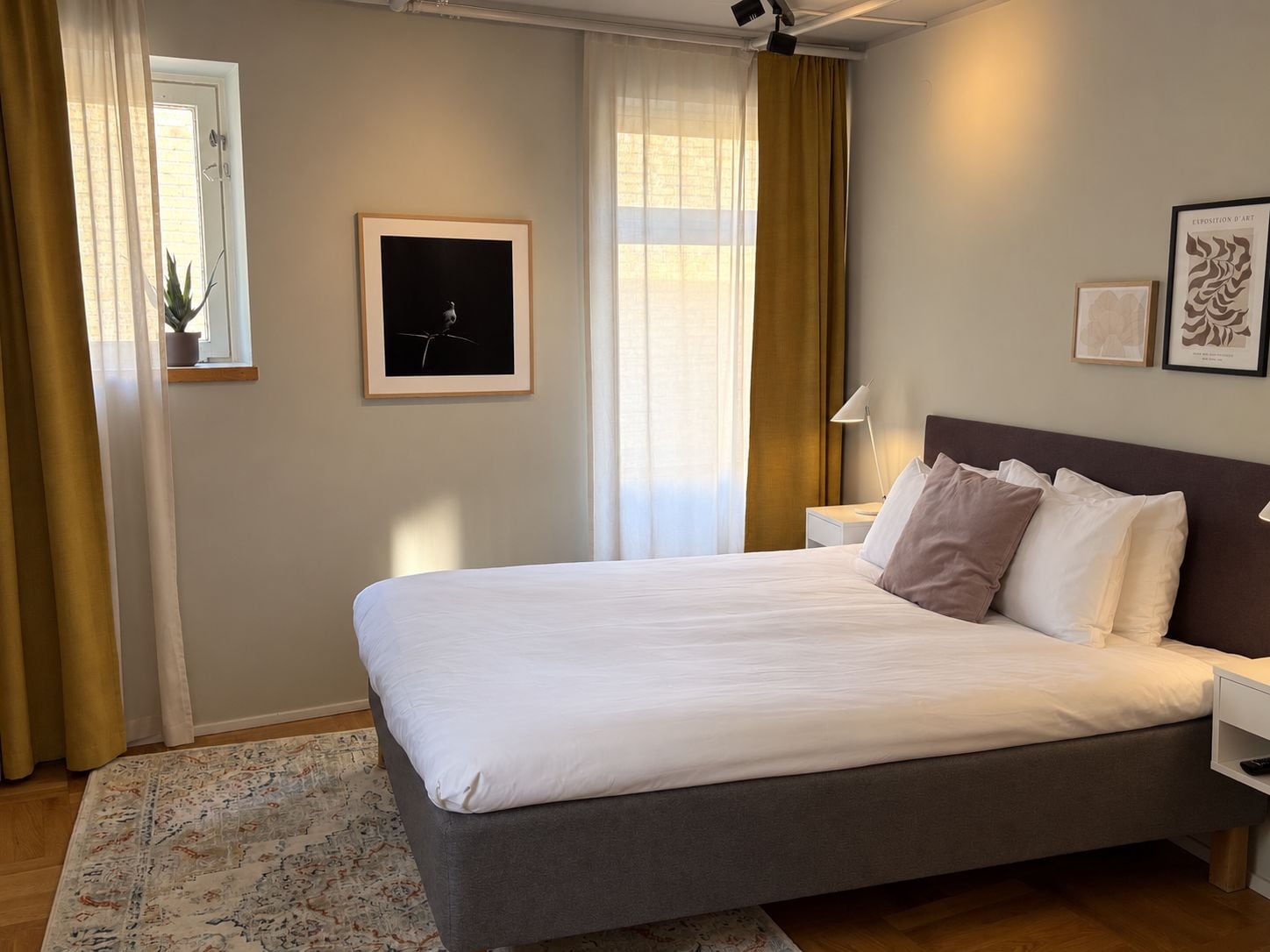 Habitación de hotel con una cama grande, una mesita de noche, una planta en maceta y una obra de arte enmarcada en la pared.