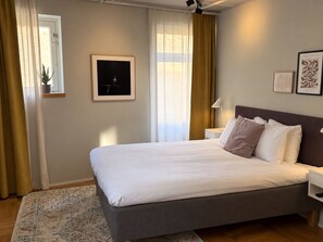 A hotel room with a large bed, a bedside table, a nightstand, a potted plant, and a framed artwork on the wall. - Second Home Hotel & Apartments (Solna)