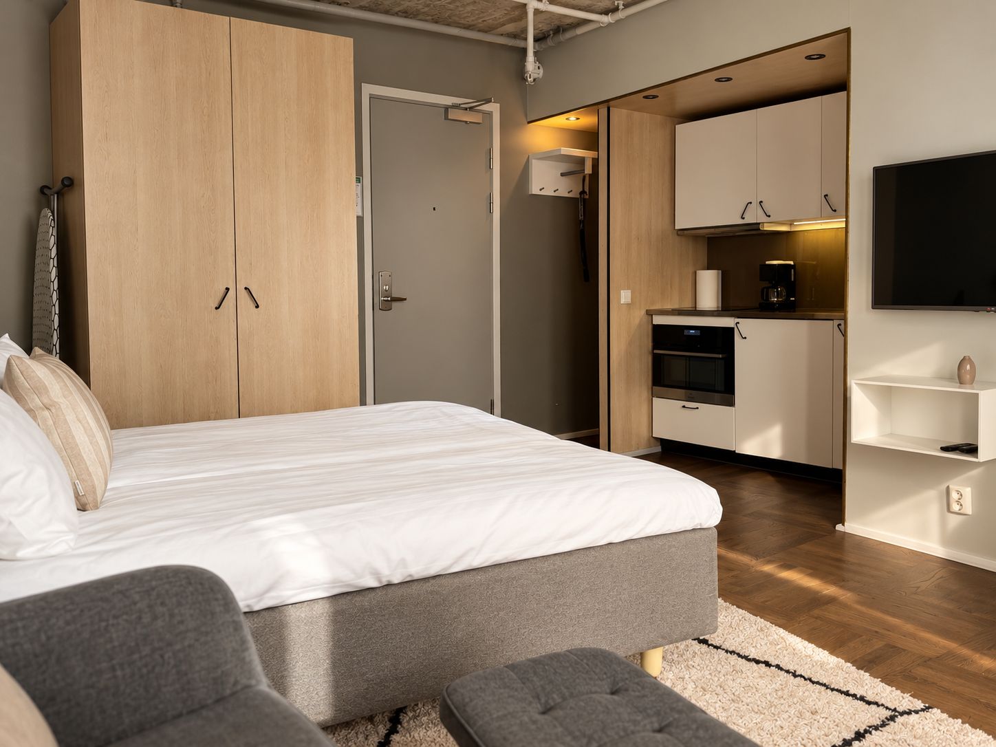 A modern bedroom with a bed, a wardrobe, a kitchenette, and a TV.