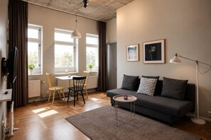 Una sala de estar moderna con un sofá gris, una mesita redonda, una zona de comedor con una mesa blanca y sillas, y un radiador.