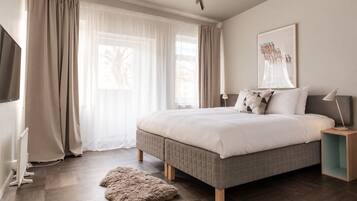 Un dormitorio con cama, cortinas, alfombra, mesita de noche y lámpara de pared.