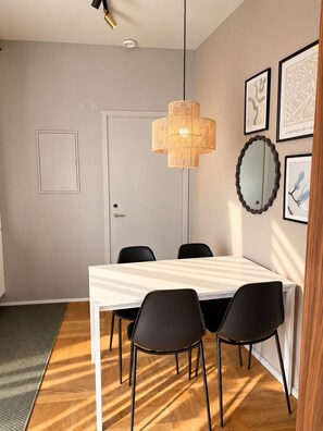 A dining area with a white table, black chairs, a woven pendant light, and framed artwork on the wall. - Second Home Hotel & Apartments (Solna)