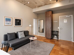 A modern living room with a grey sofa, a small round table, and a mirror. - Second Home Hotel & Apartments (Solna)