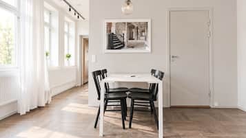 En matplats med ett vitt bord och svarta stolar, en inramad tavla på väggen och en dörr till höger.
