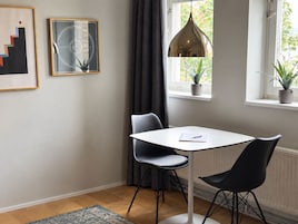 A modern dining area with a white table and two black chairs, a pendant light, and two framed artworks on the wall.