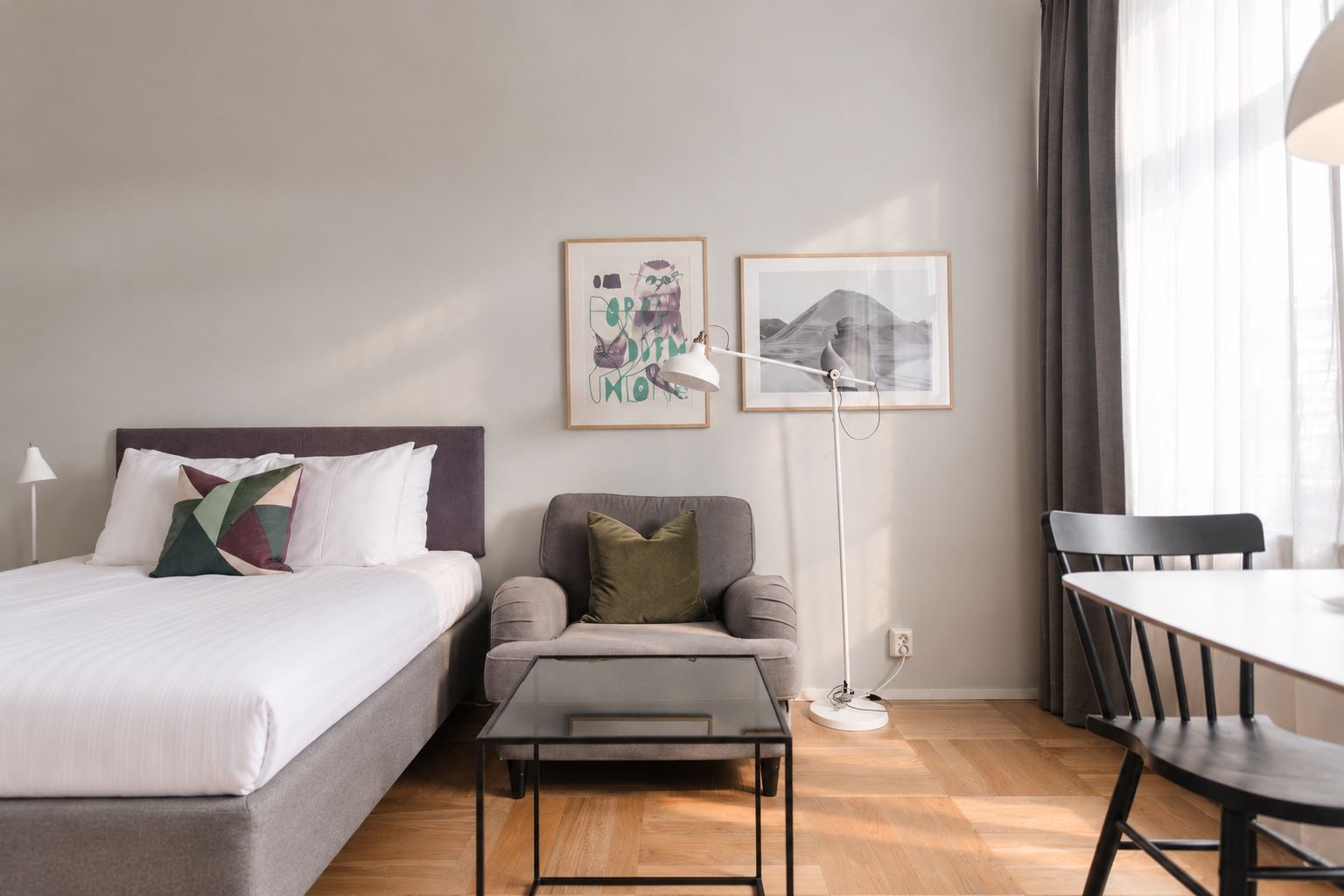 A hotel room with a bed, a sofa, a small table, a desk, and two framed pictures on the wall.
