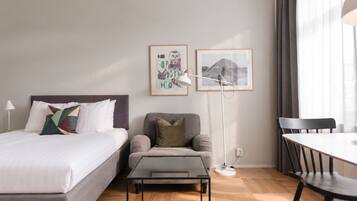 A hotel room with a bed, a sofa, a small table, a desk, and two framed pictures on the wall.