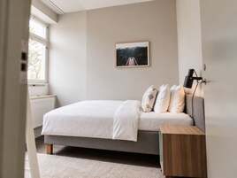 Un dormitorio con cama, mesita de noche y ventana.