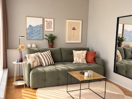 A modern living room with a green sofa, a coffee table, and a large mirror.